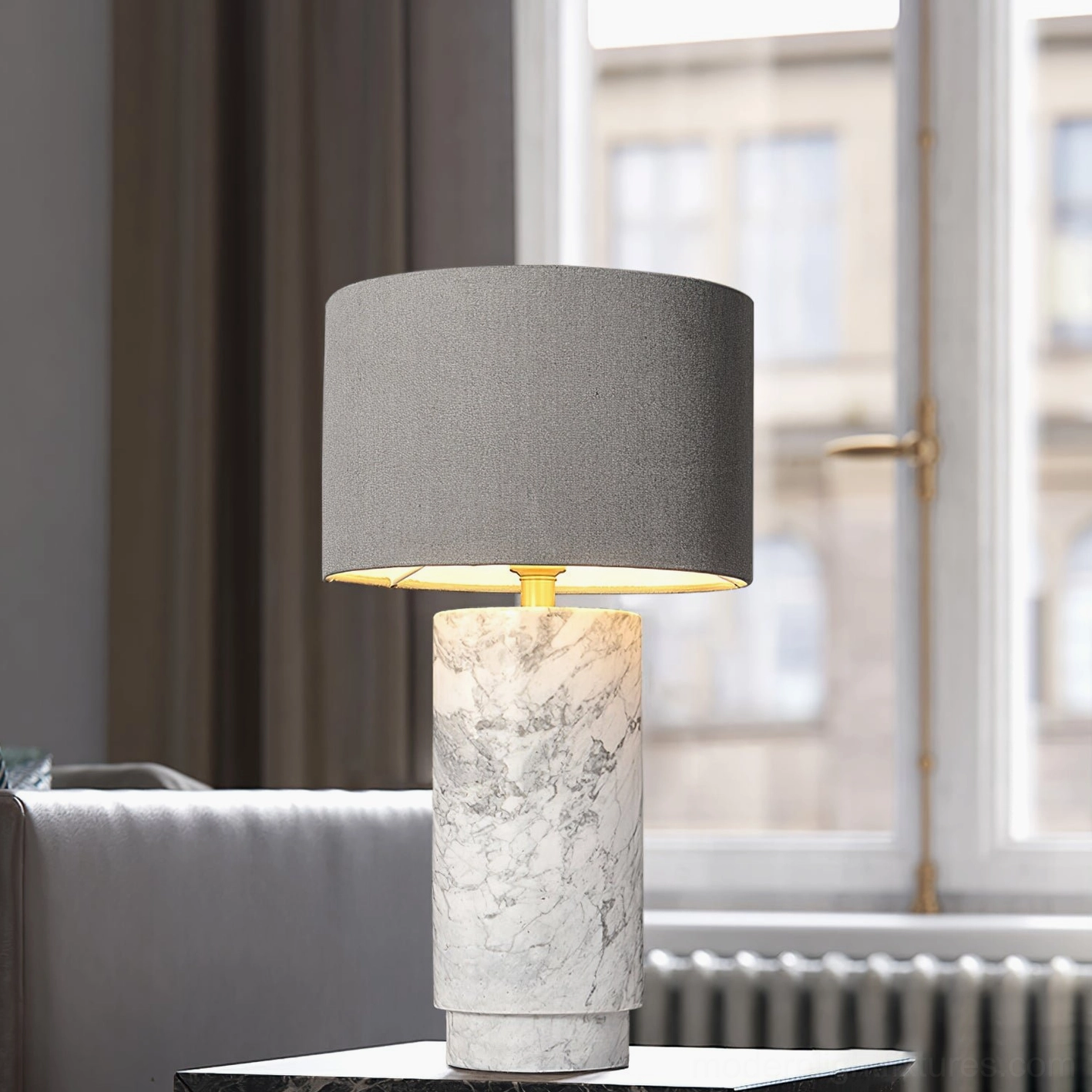 Cylindrical marble table lamp with grey fabric shade and white veined stone base by window, three-quarter angle view
