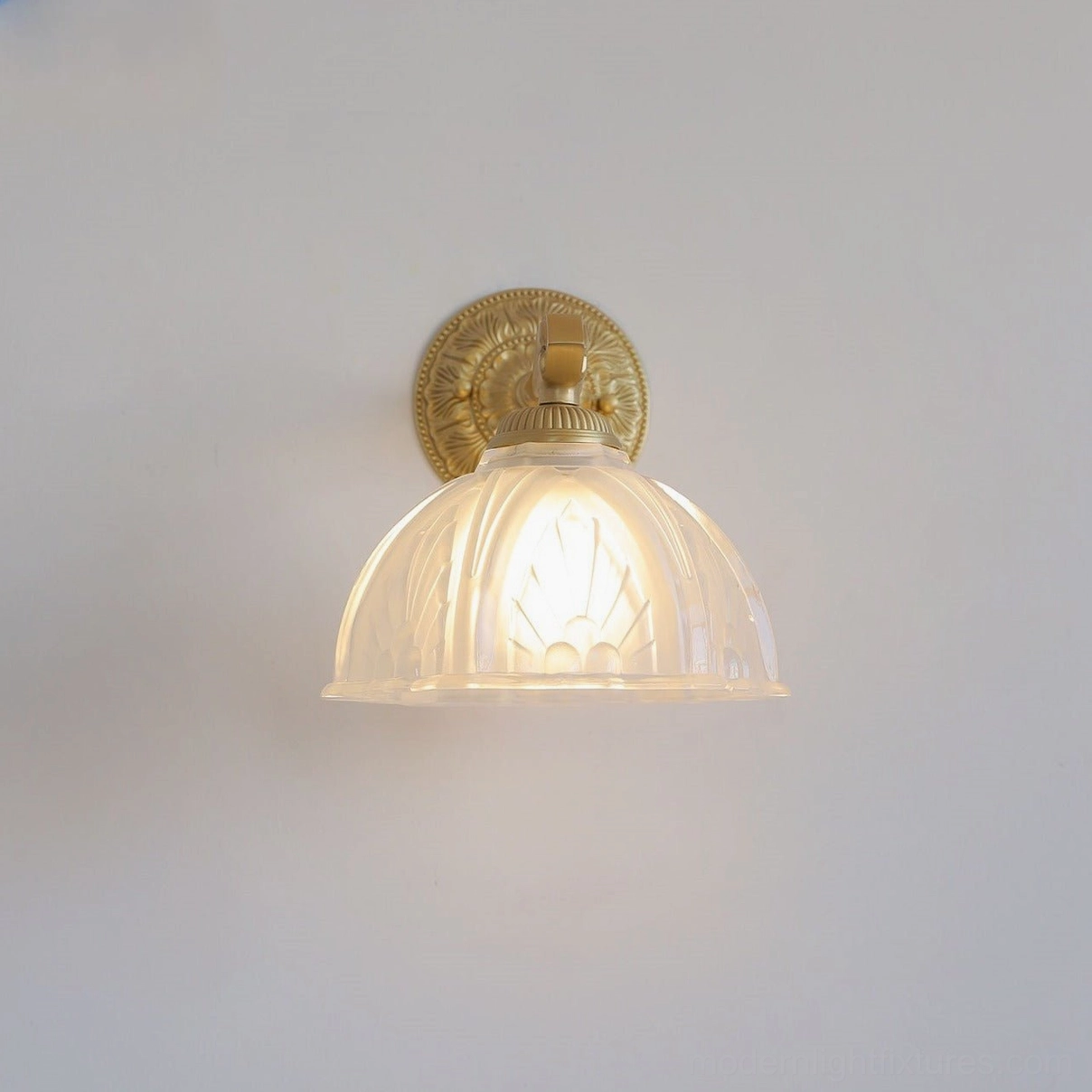 Marceau brass wall sconce close-up front view of illuminated embossed backplate and fluted frosted glass dome shade
