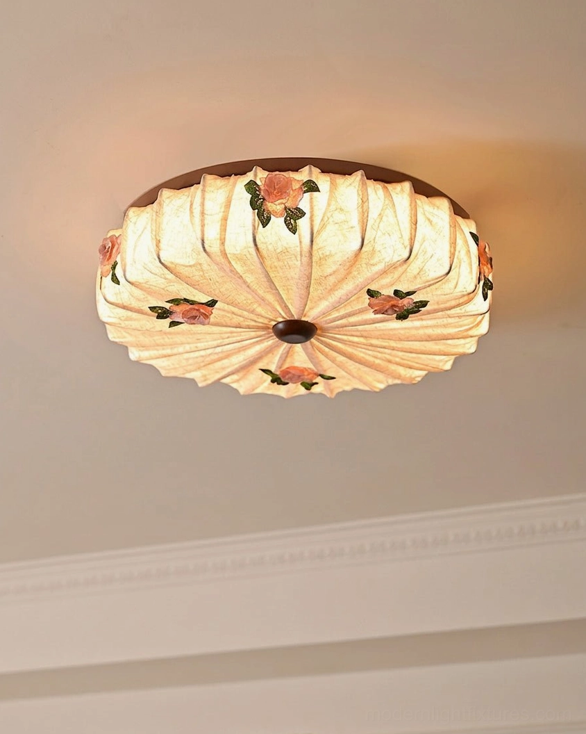 Maribelle fabric flush mount illuminated from below showing pleated shade structure, rose details, and warm ambient glow