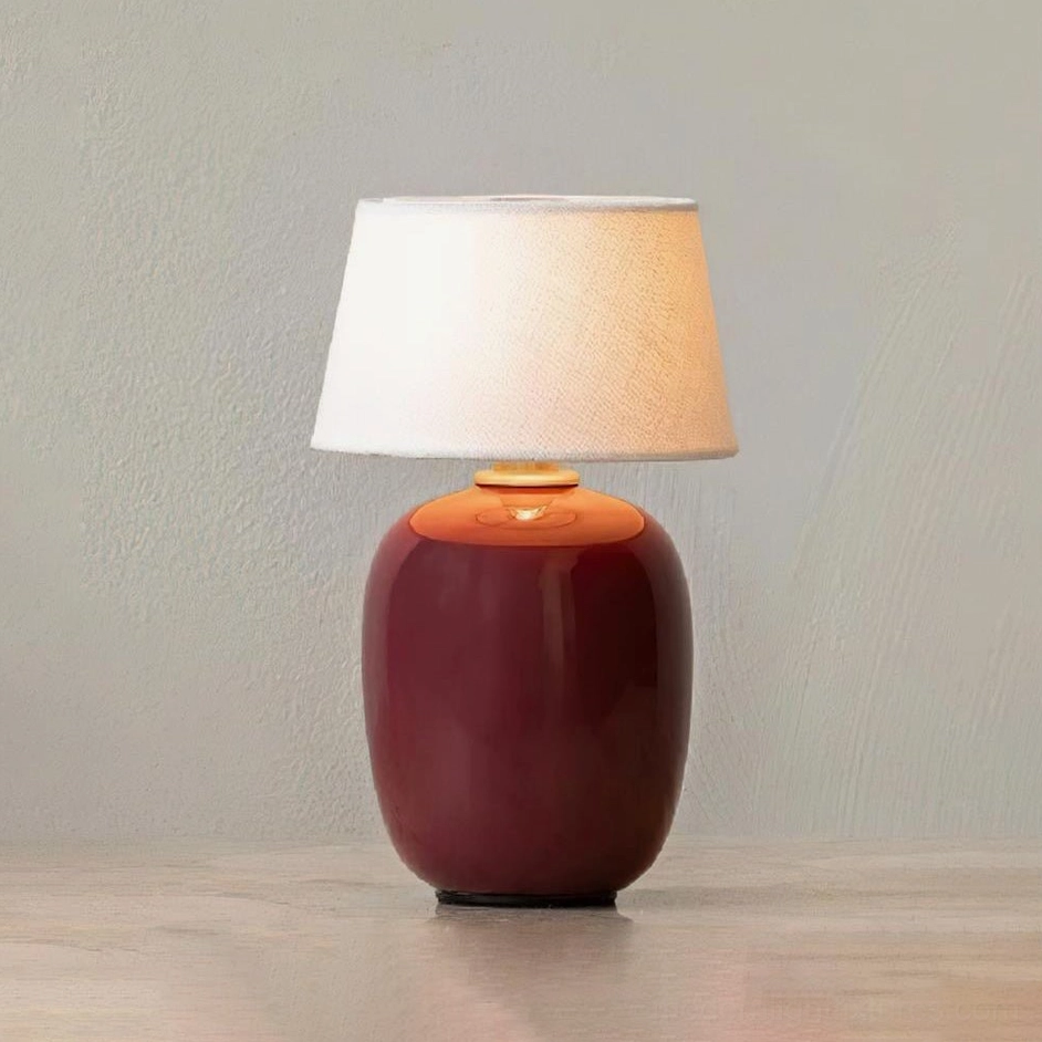 Deep burgundy wine-red ceramic table lamp with beige fabric shade on wooden table – warm interior lighting