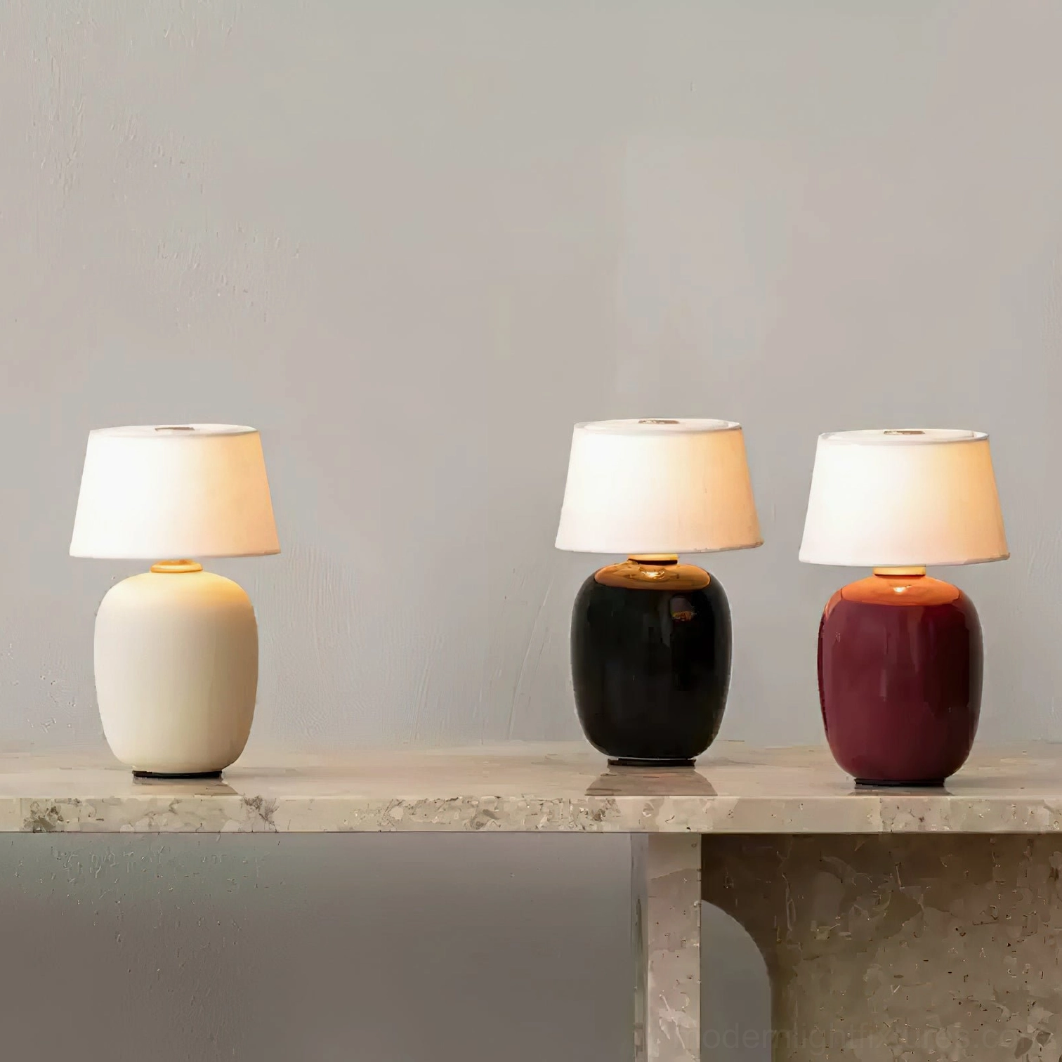 Three modern ceramic table lamps in sand, black, and burgundy finishes displayed together on marble console – interior styling inspiration