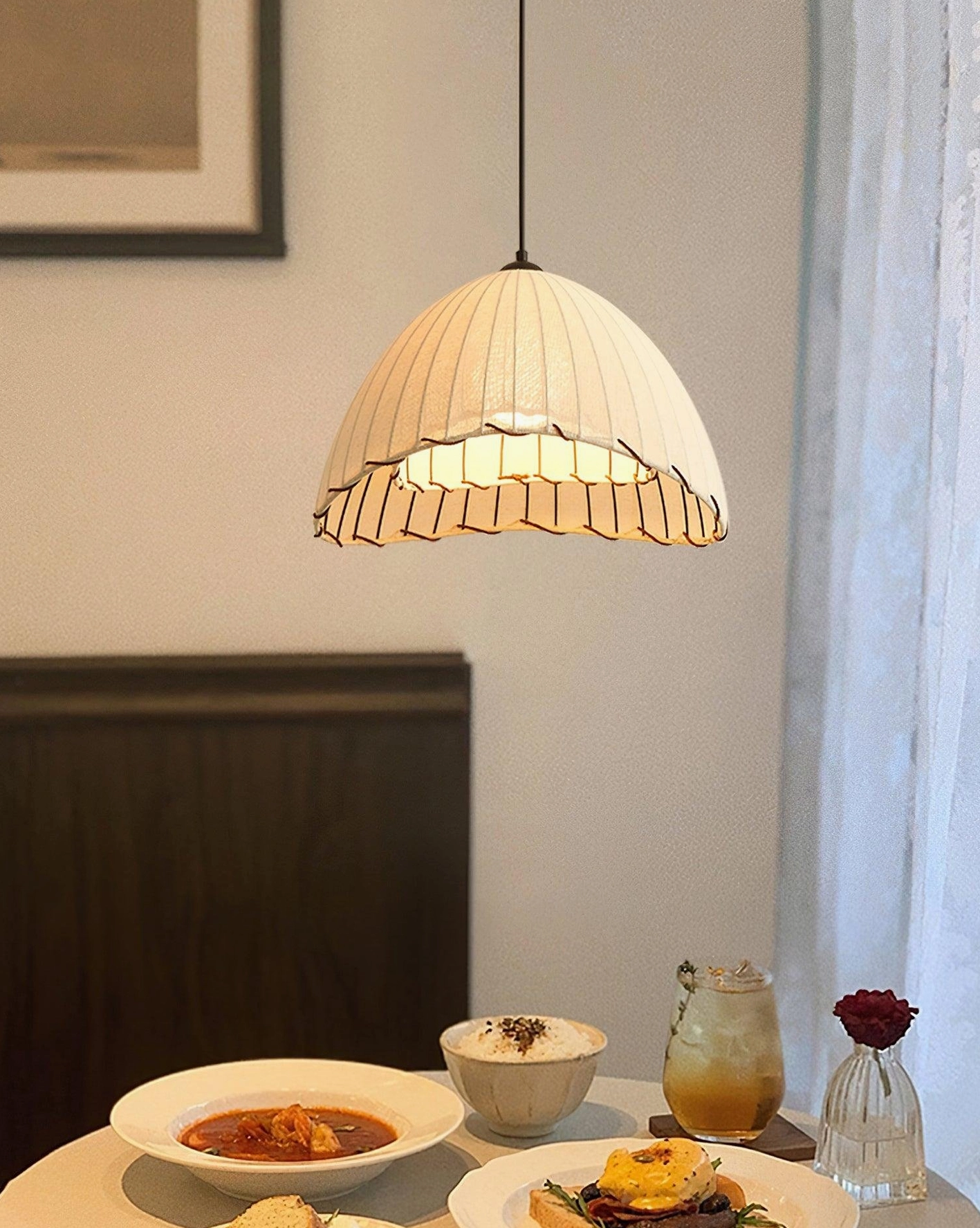 Close-up eye-level view of Maris pleated linen pendant light over casual dining table setting