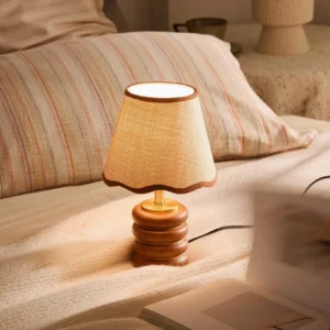 Lit Marlowe mid-century table lamp on bedroom nightstand beside striped bedding, warm ambient glow illuminating pillow