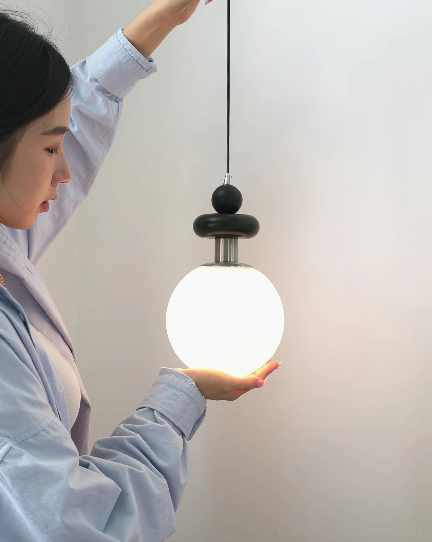 Marra Globe Pendant Light featured in minimalist interior space with woman showcasing the modern pendant design and proportions
