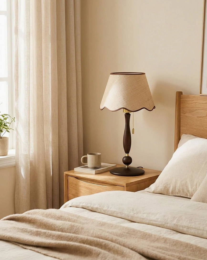 Master bedroom nightstand scalloped table lamp illuminated beside wooden bed frame with sheer linen curtains and soft lighting - three-quarter front