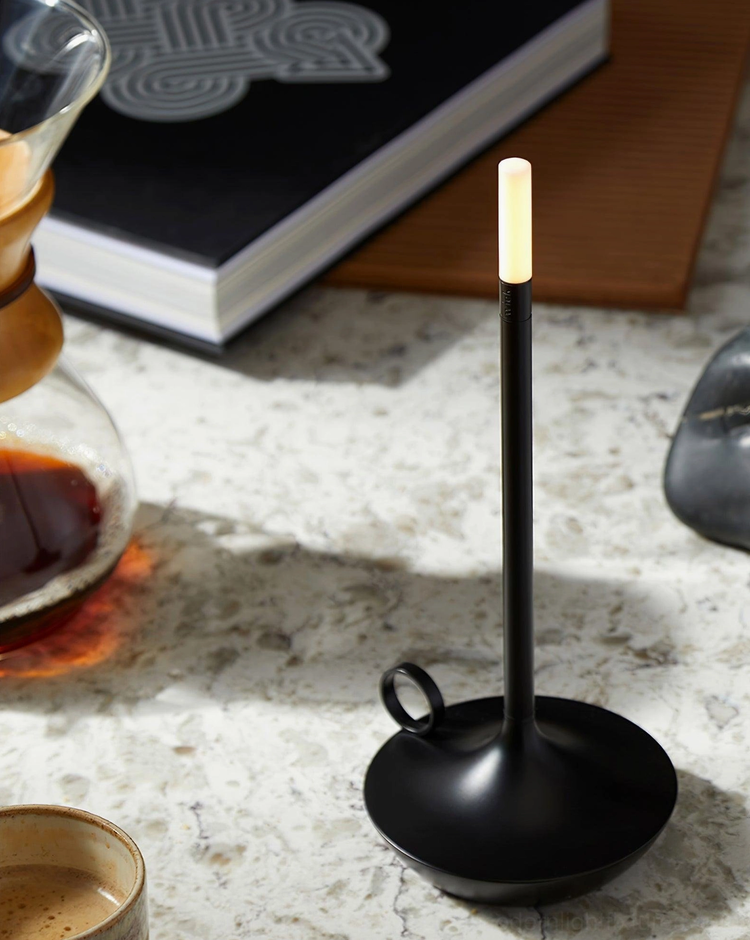 Matte black LED candle table lamp on marble surface styled with coffee cup and book, contemporary interior styling