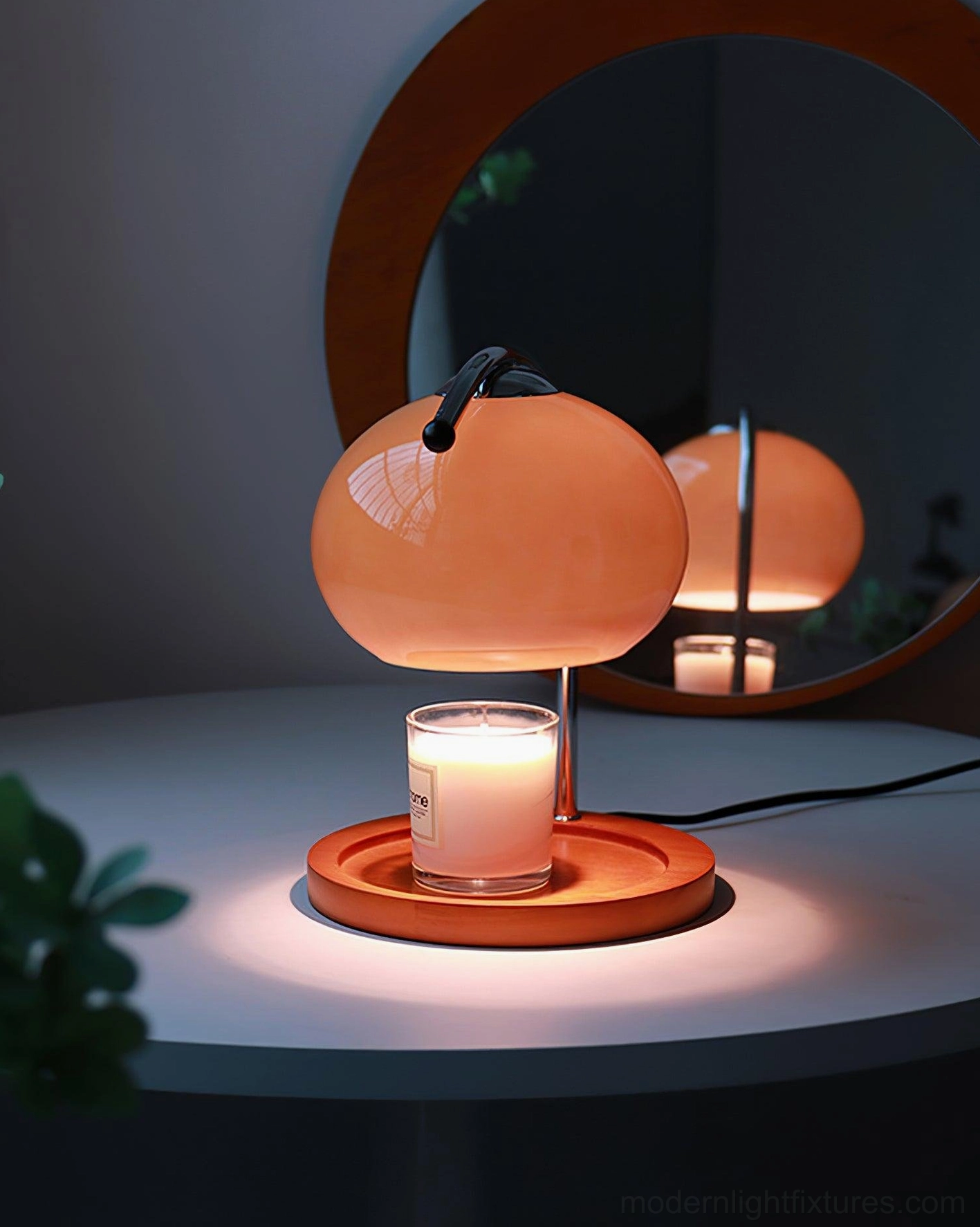 Mauri candle warmer lamp with peach pink glossy shade on dark grey side table with mirror, warm halogen illumination