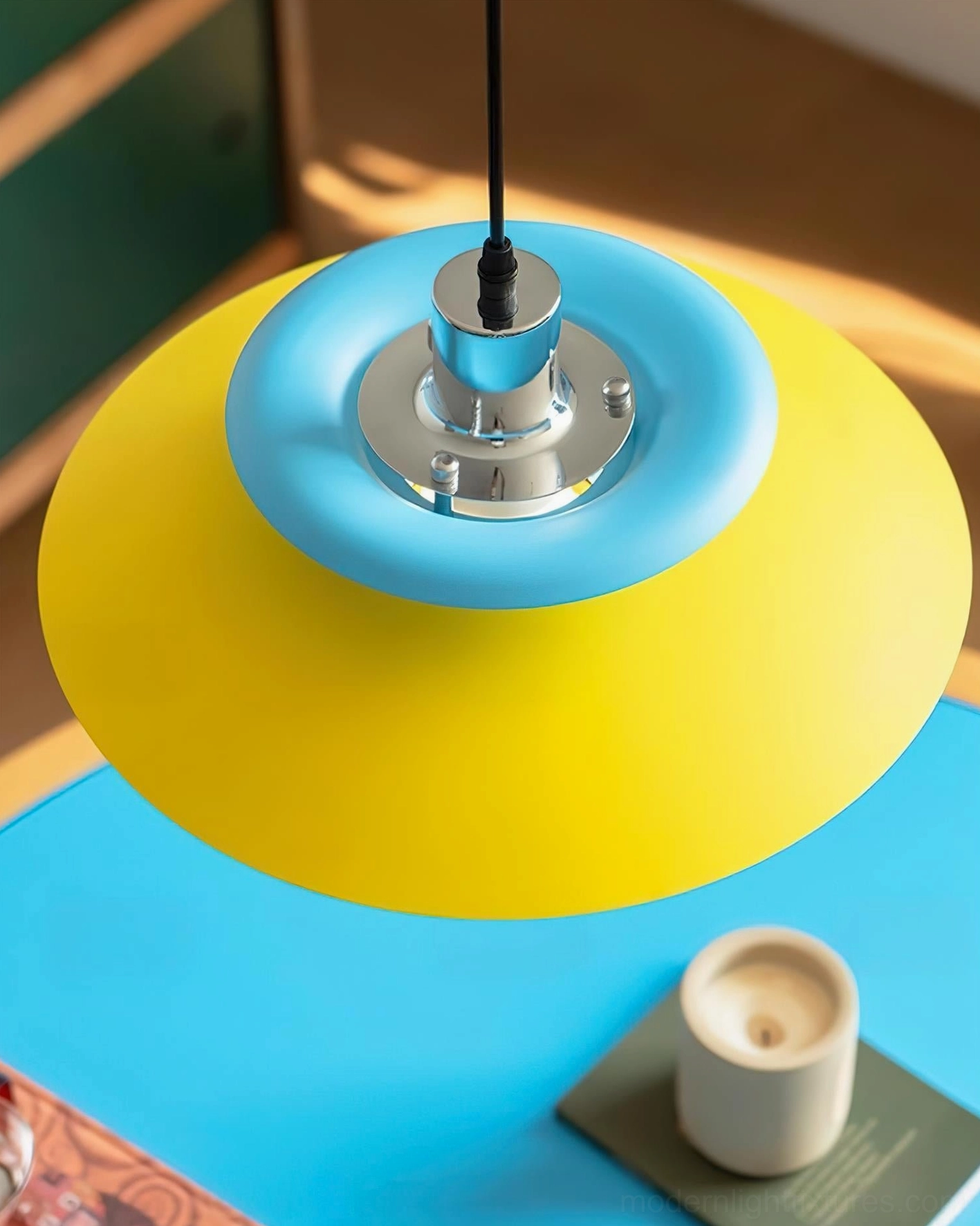 Close-up bottom view of Mellowe pendant lamp showing chrome socket, cyan and yellow matte disc layers, tabletop setting