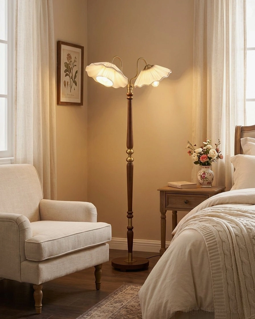 Merritt two-light floor lamp positioned in bedroom with lounge chair, showcasing independently adjustable brass gooseneck arms and warm vintage ambiance