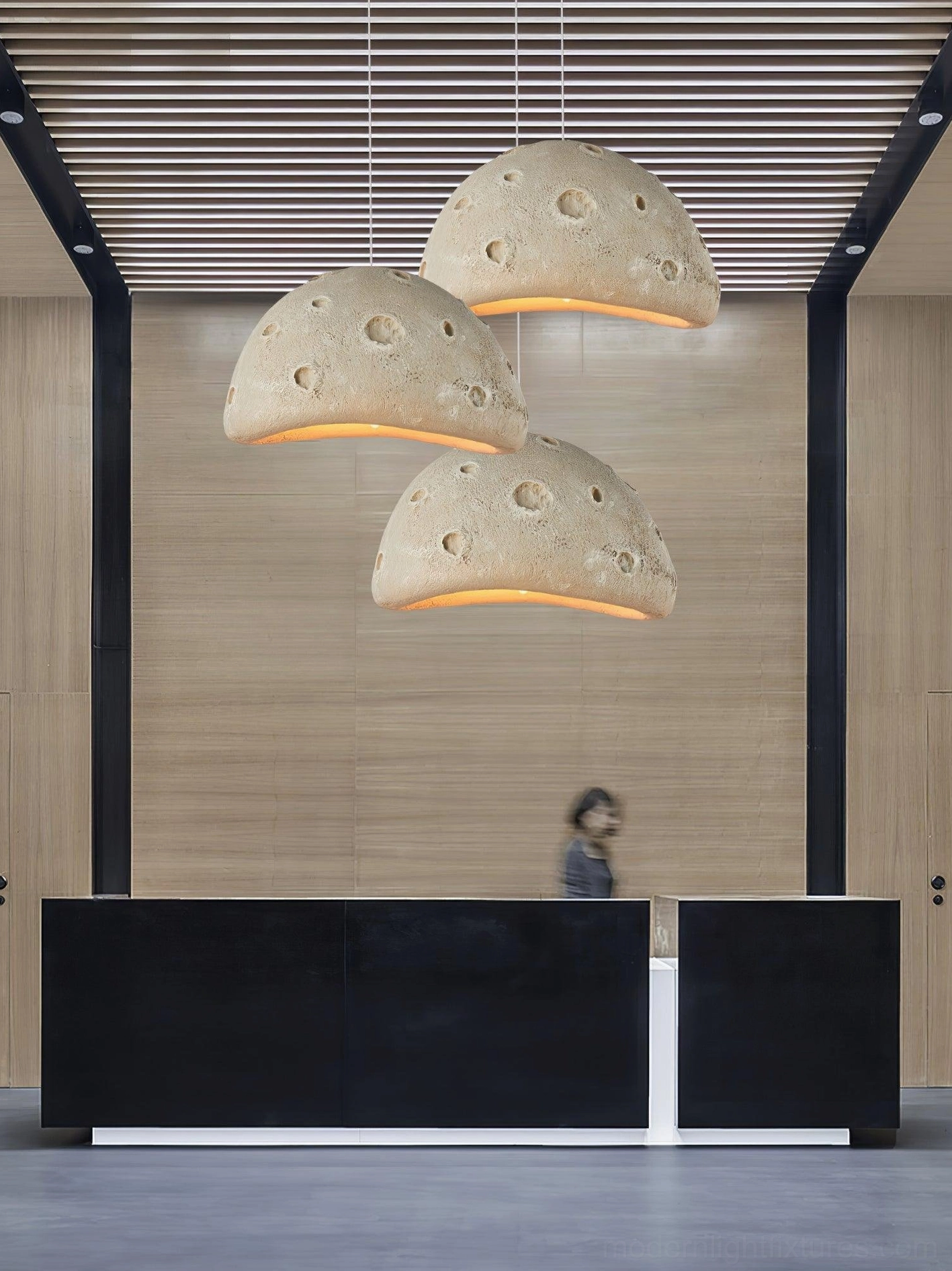 Set of three beige meteorite crater pendant lights illuminating hotel lobby reception area with wooden slat ceiling