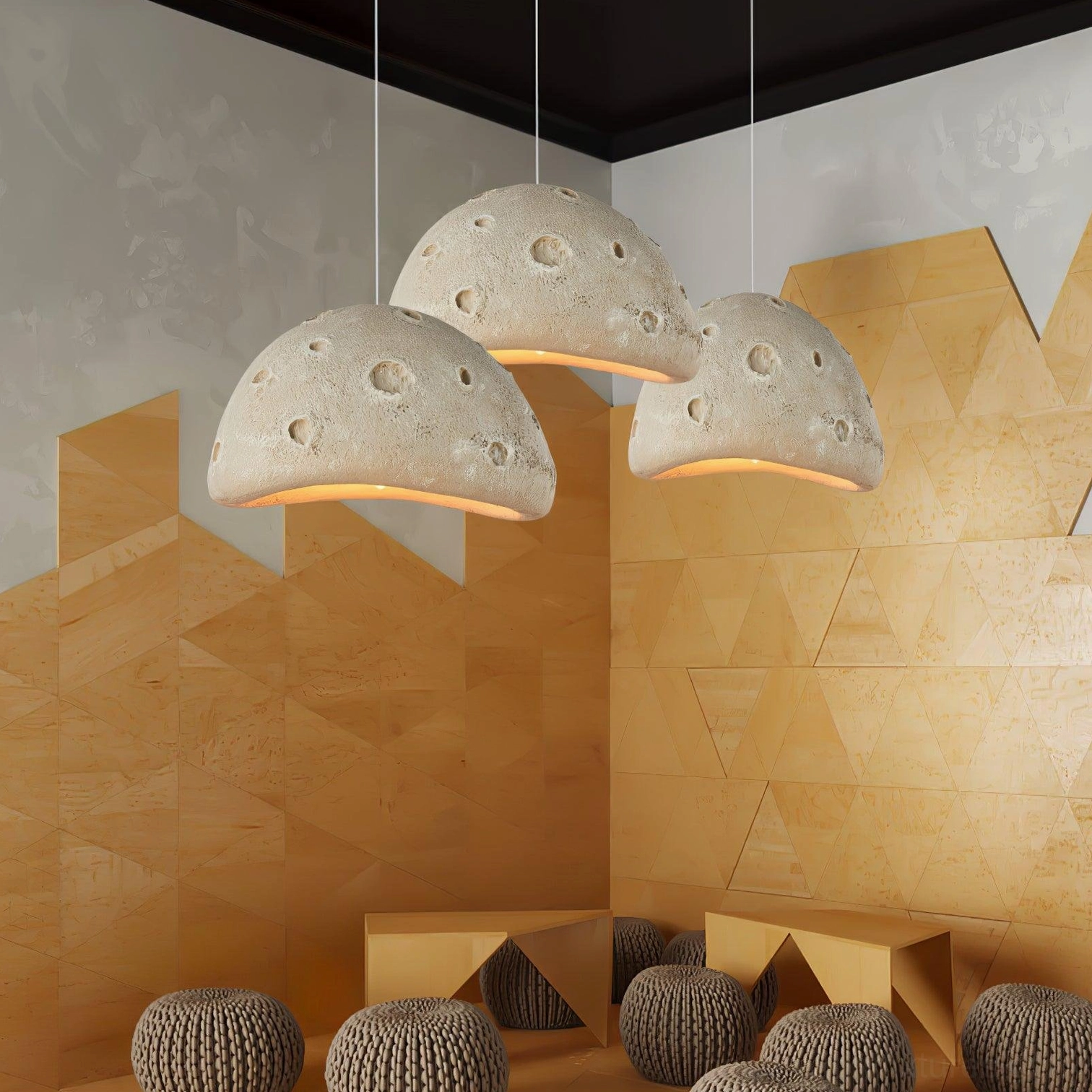 Three meteorite crater pendant lights in beige suspended in modern minimalist lounge with geometric wood wall and knitted floor cushions