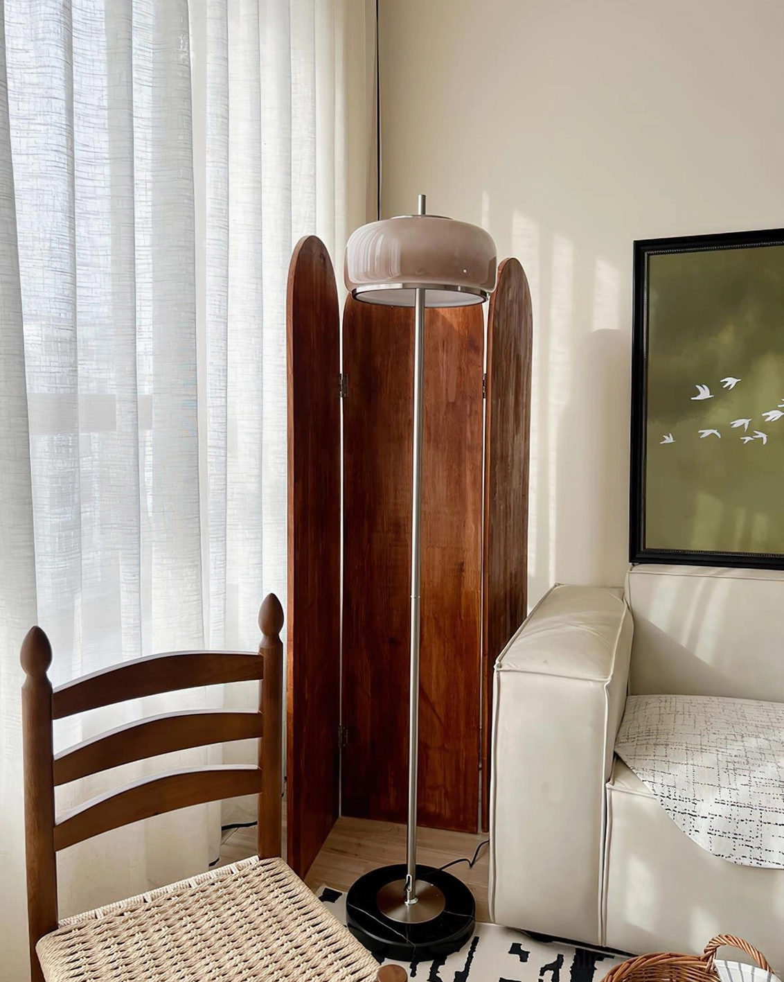 Mid-century modern mushroom floor lamp with taupe shade and black base in sunlit retro living room with wooden screen