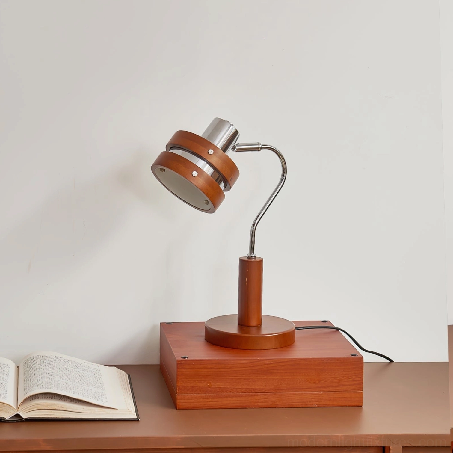 Modern industrial table lamp positioned on wooden desk surface with open book, rear three-quarter view