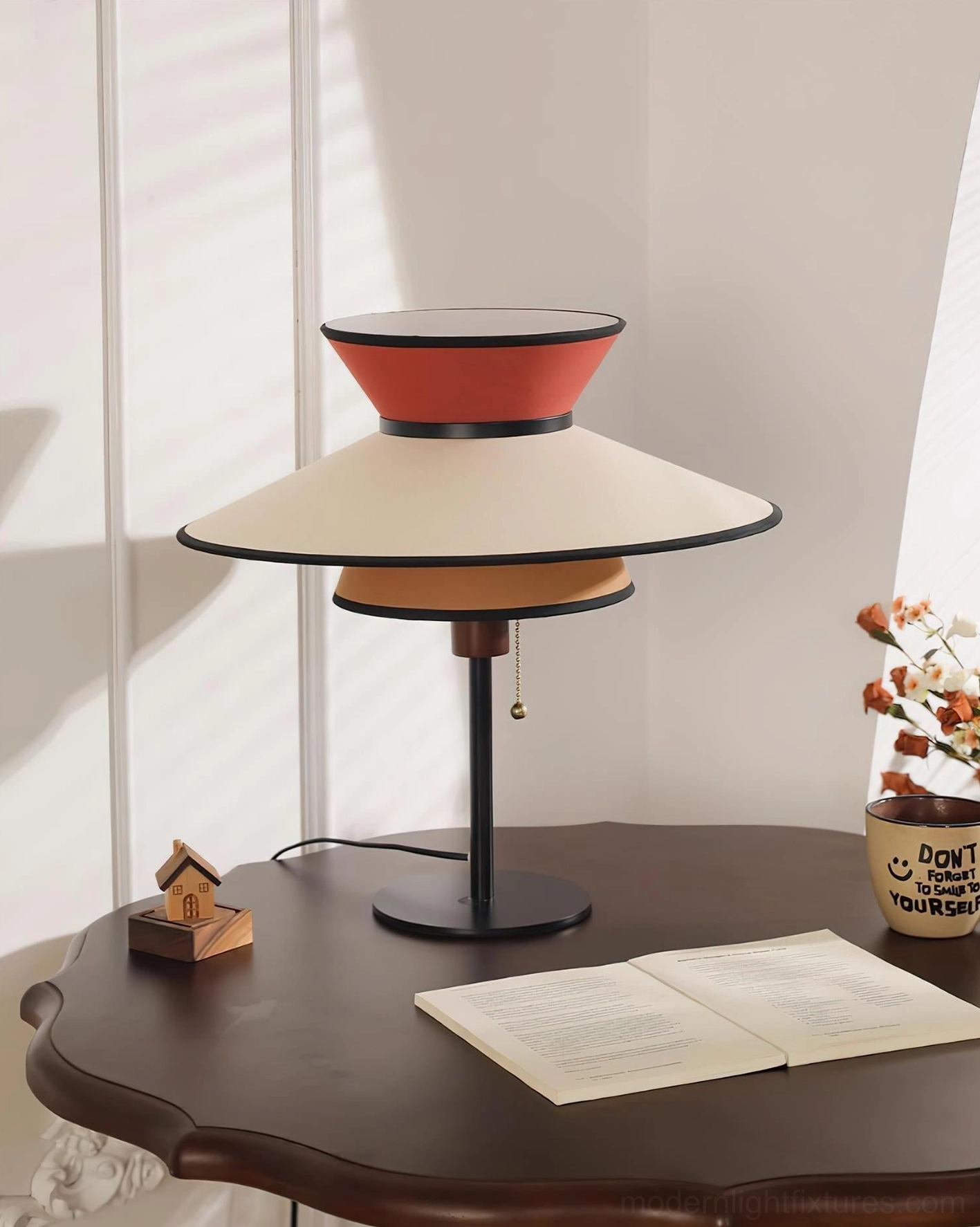 Mid-century modern table lamp with stacked conical shades on home office side table beside open book and decorative elements