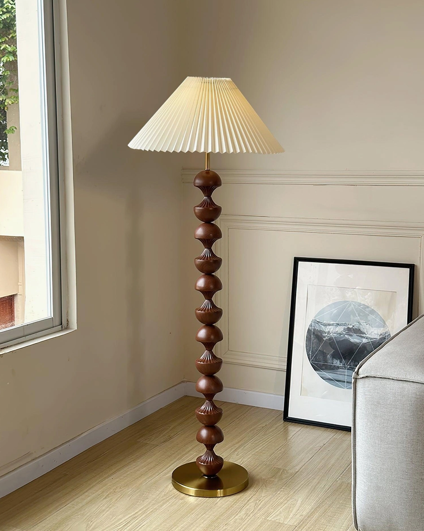 Dark brown stacked wood pole floor lamp three-quarter side view in mid-century modern living room with wall artwork, brass metal base
