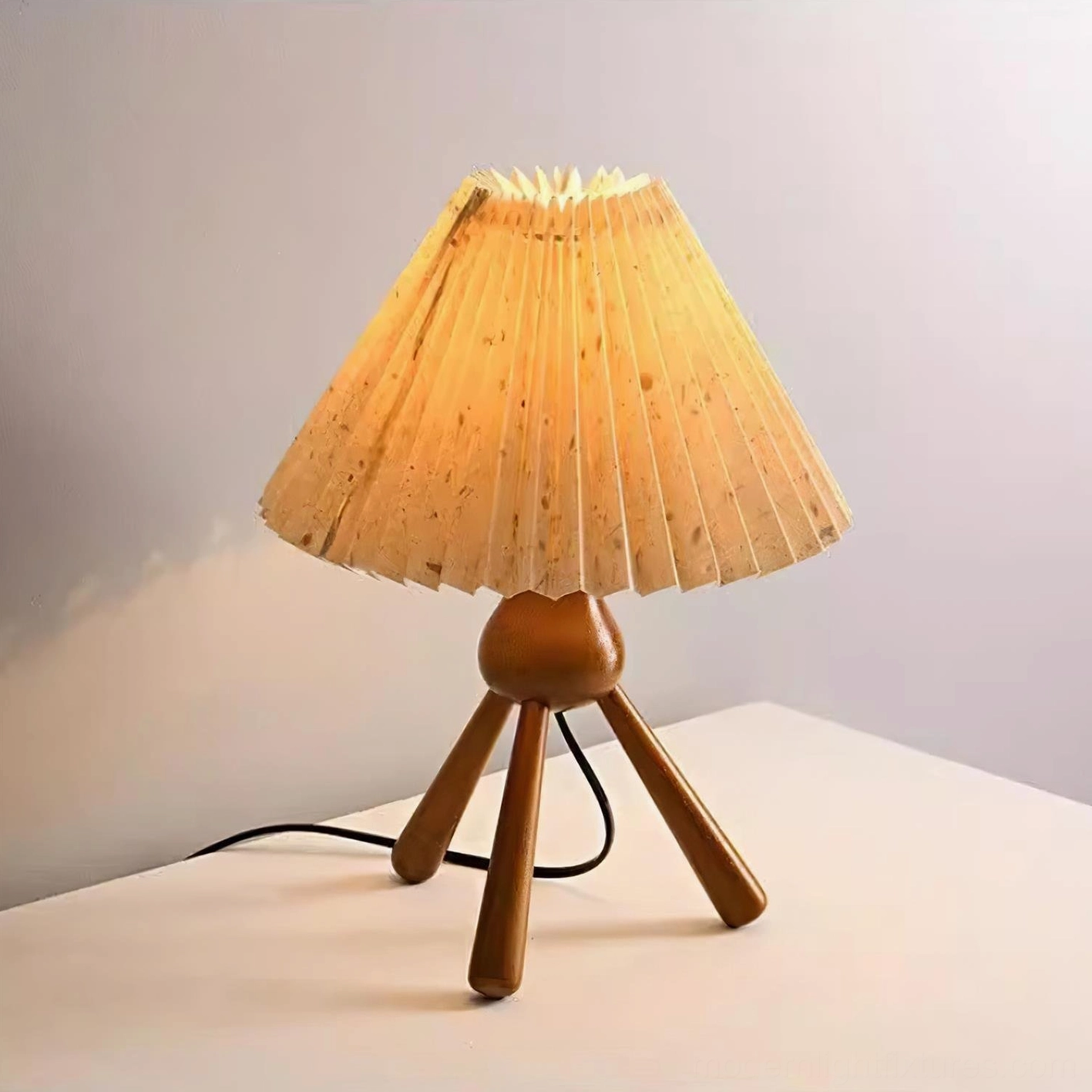 Mid-century modern pleated table lamp with glowing warm shade and wood tripod base silhouette