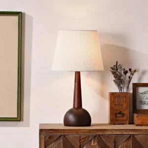 Modern wooden table lamp displayed on vintage dresser with wall art and dried flowers, three-quarter angle