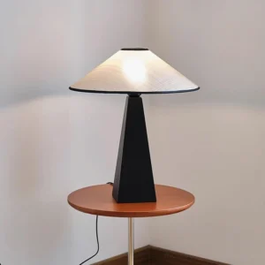 Lit natural fiber table lamp on wooden nightstand in modern bedroom setting, warm diffused light