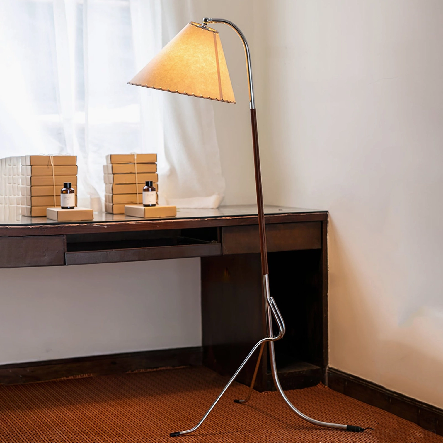 Mid-century tripod floor lamp positioned in home desk corner with woven area rug, showing adjustable curved metal arm for directional lighting control