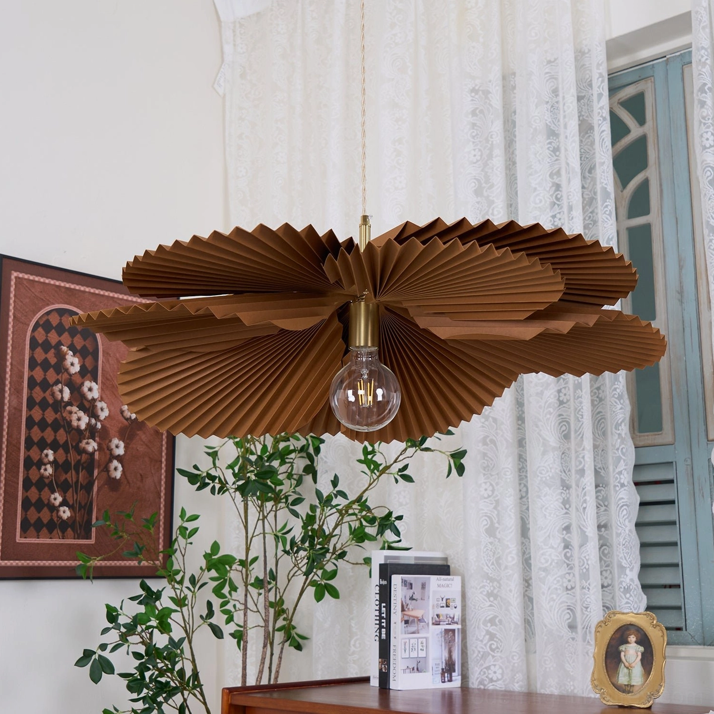 Brown pleated pendant fixture with exposed Edison bulb in vintage interior with lace curtains and desk accessories