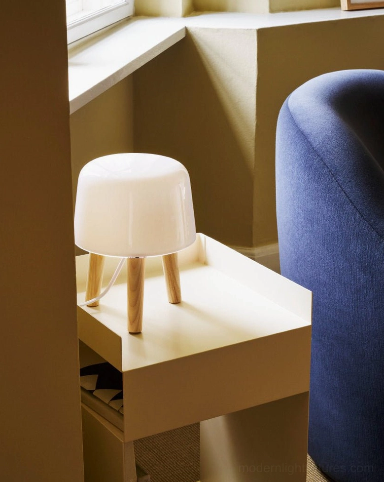Side view of compact milk glass table lamp positioned beside blue fabric sofa on windowsill, showcasing versatile placement
