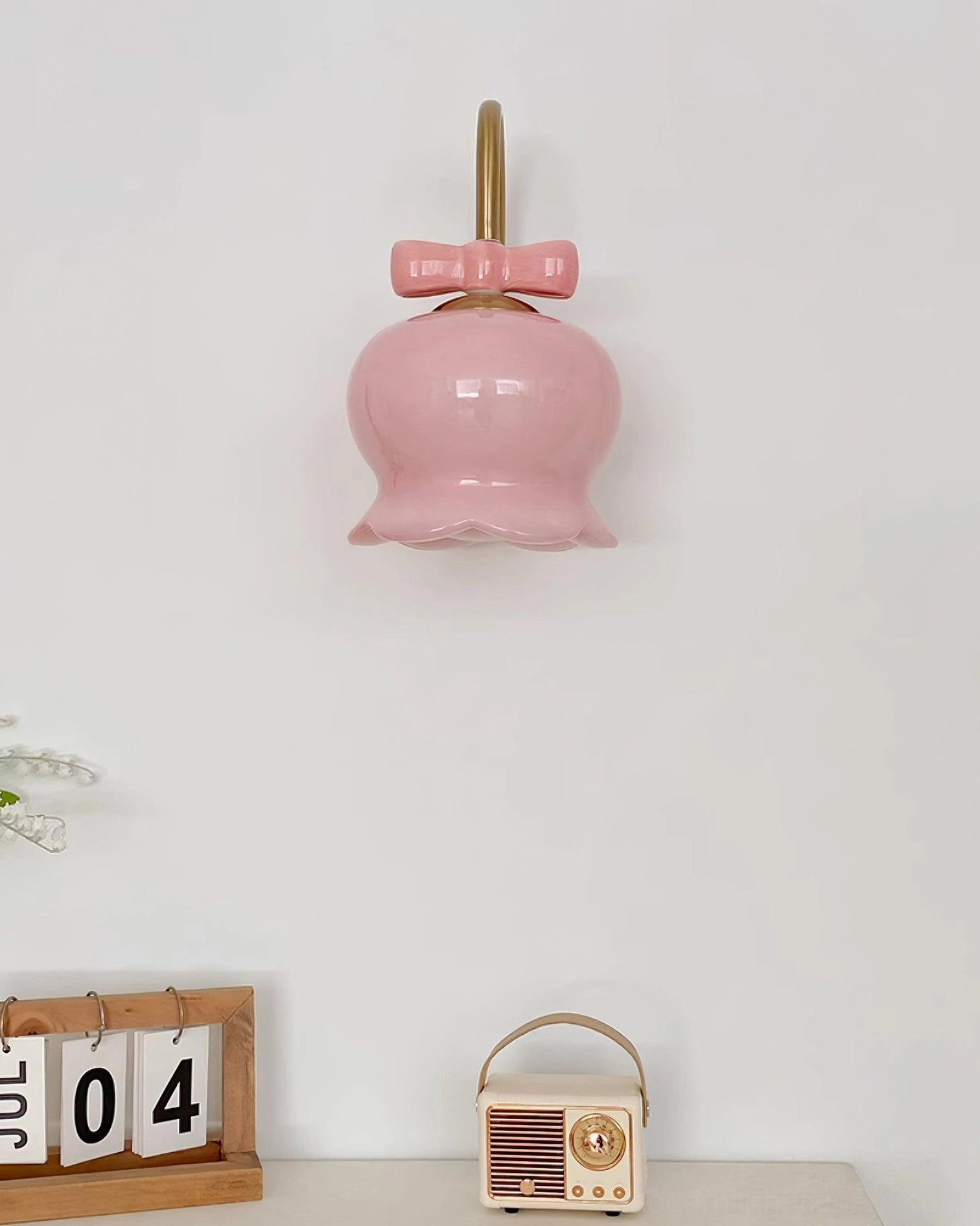 Solid pink ceramic Millie Bells wall sconce with brass metal frame and bow decoration, mounted on wall near home office desktop