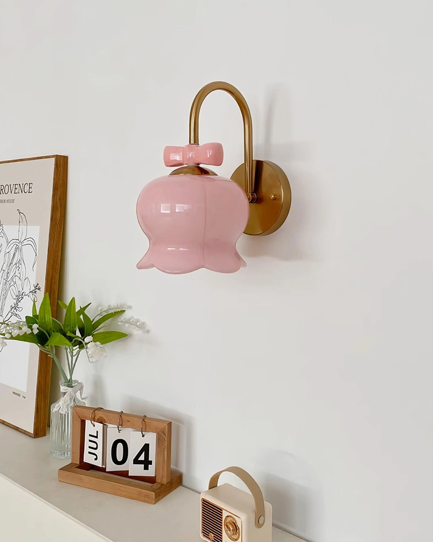 Pink ceramic Millie Bells wall sconce with brass metal bracket and girly bow detail mounted on cozy home interior wall