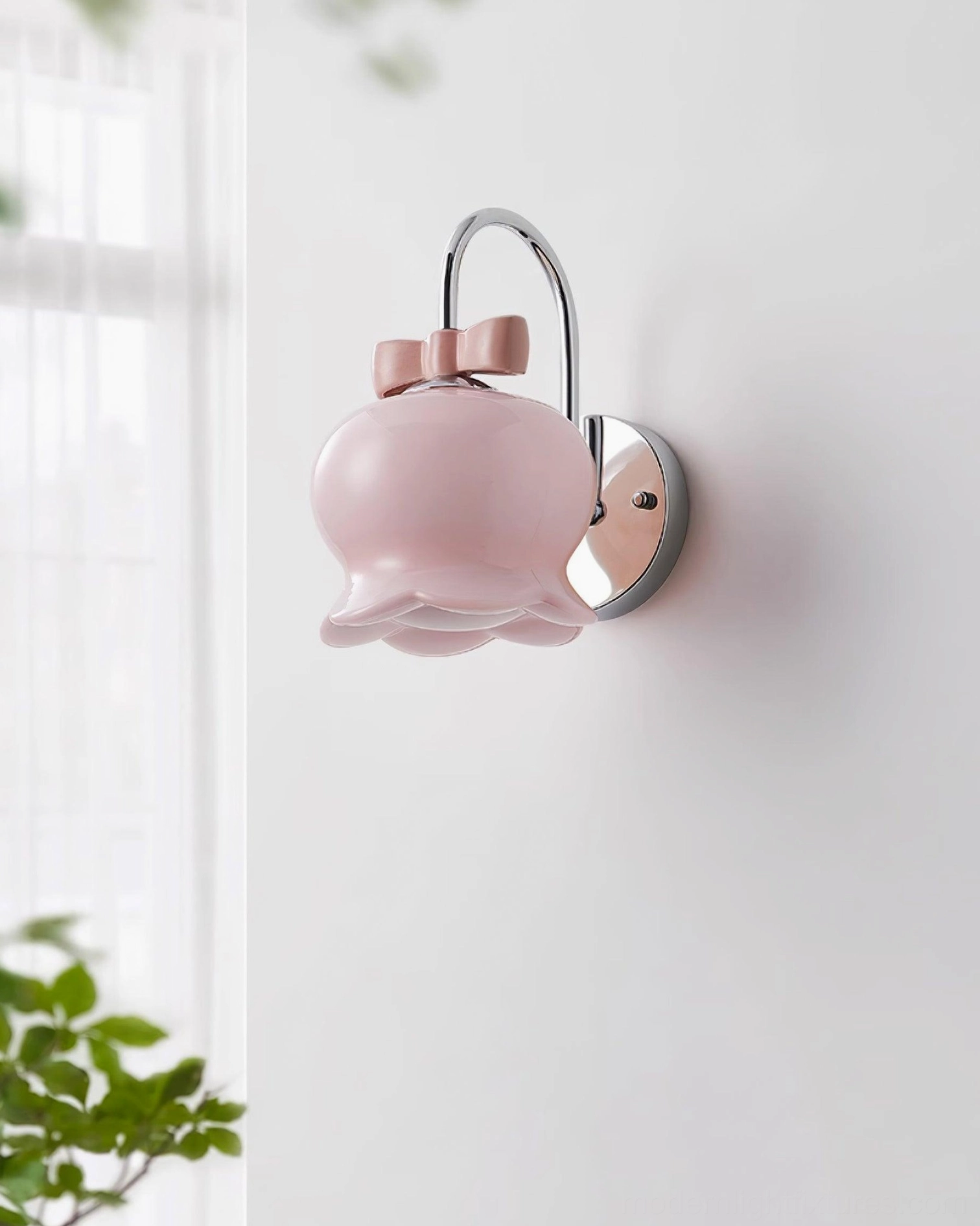 Pink ceramic bell-shaped wall sconce with chrome metal hardware mounted on white wall near window, Millie Bells design with bow accent