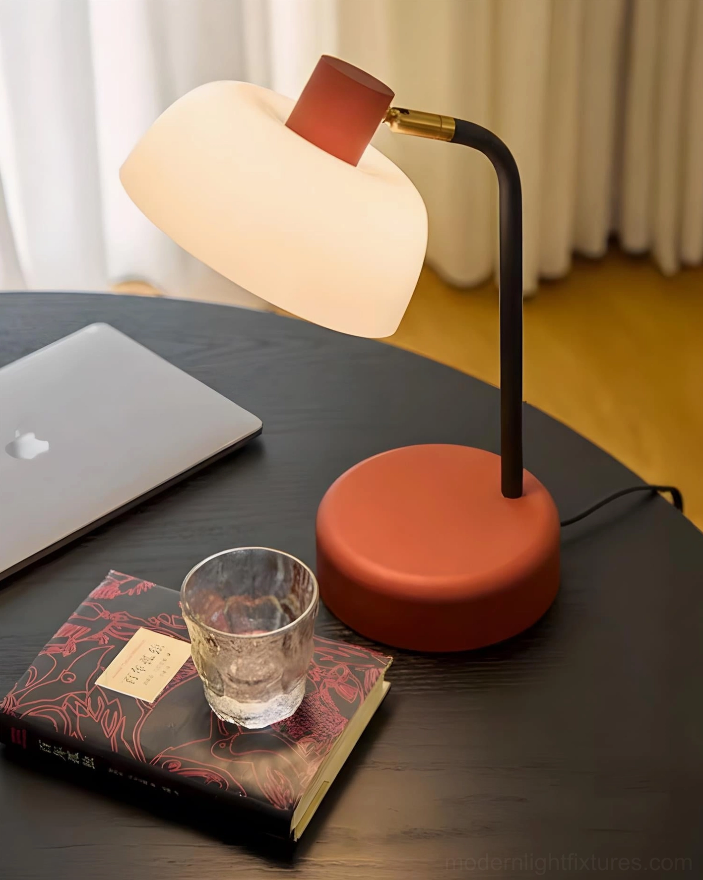 Contemporary arc desk lamp with terracotta red base in home office setting with modern furniture
