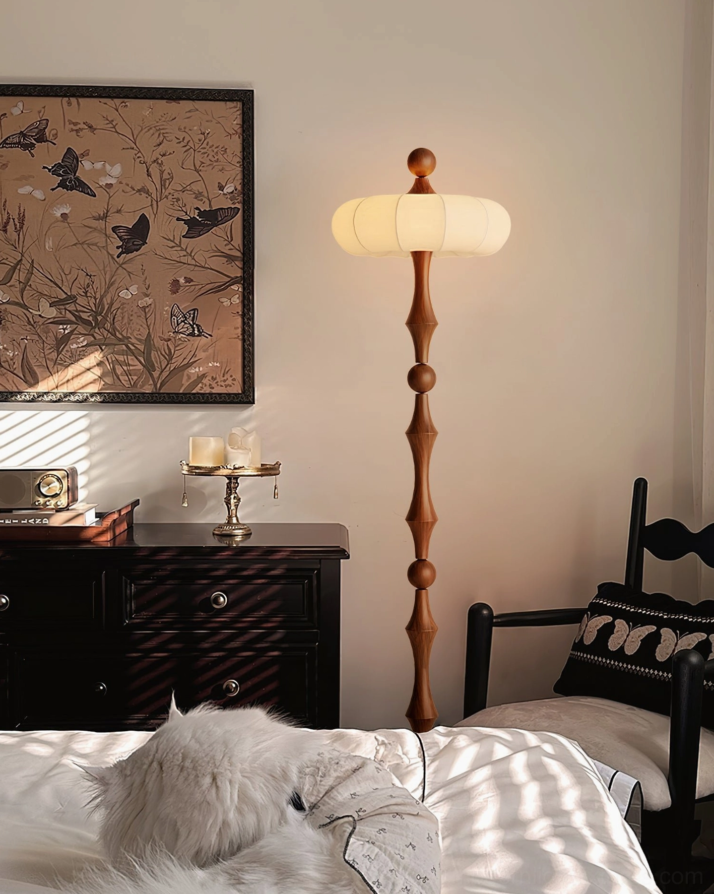Milo sculptural floor lamp in master bedroom with bed and dresser, walnut wood and lantern shade design, three-quarter side view
