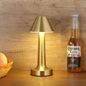Brushed gold metal Mina lamp creating warm ambient light on wooden dining table with beverages