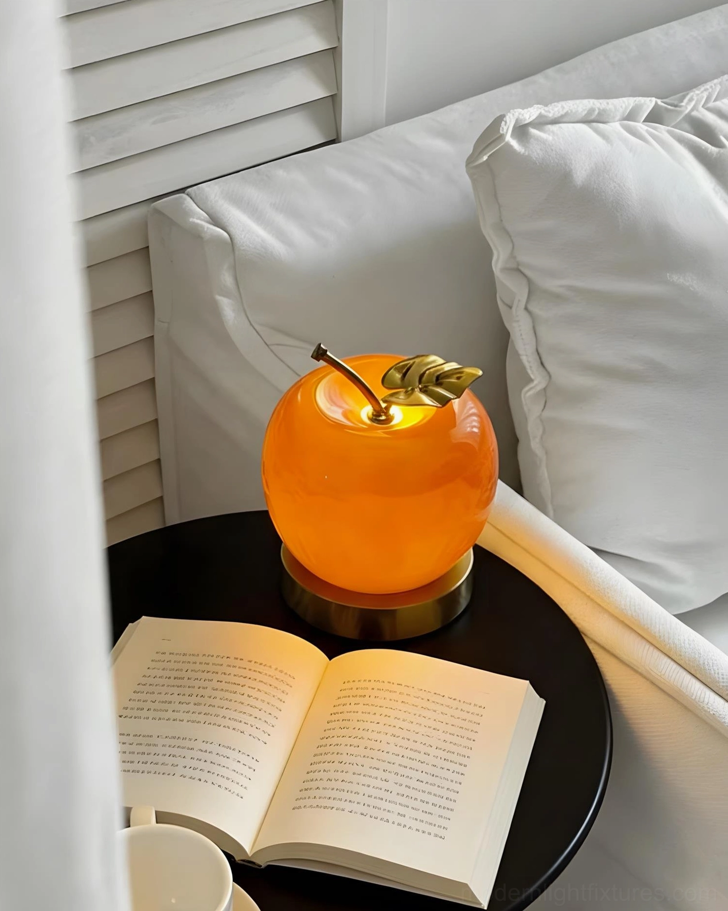 Compact orange apple table lamp on round bedside table next to open book in cozy bedroom setting