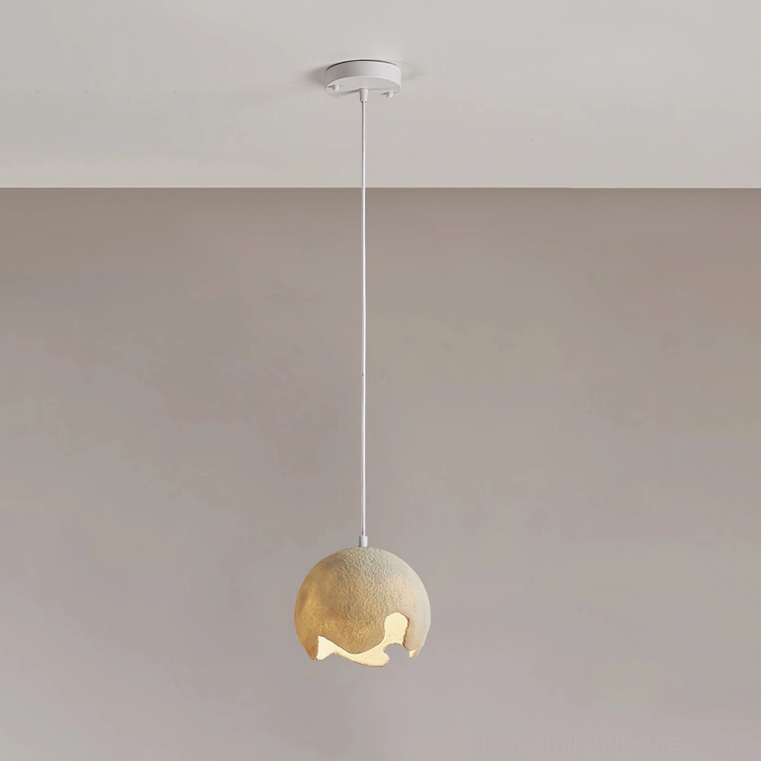 Mini beige moon crater pendant light with small matte textured shade suspended from white ceiling hardware, warm glow through cutout