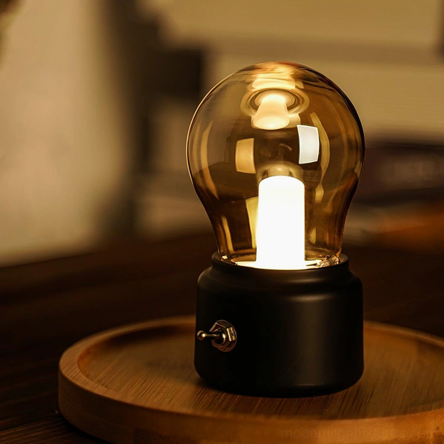 Matte black miniature bulb table lamp with amber-tinted glass on wooden tray warm lighting
