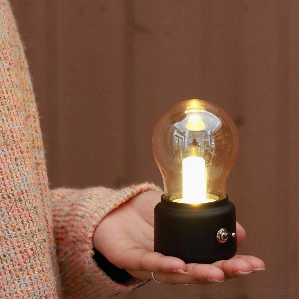 Matte black pocket-sized bulb lamp held in hand showing miniature scale and design