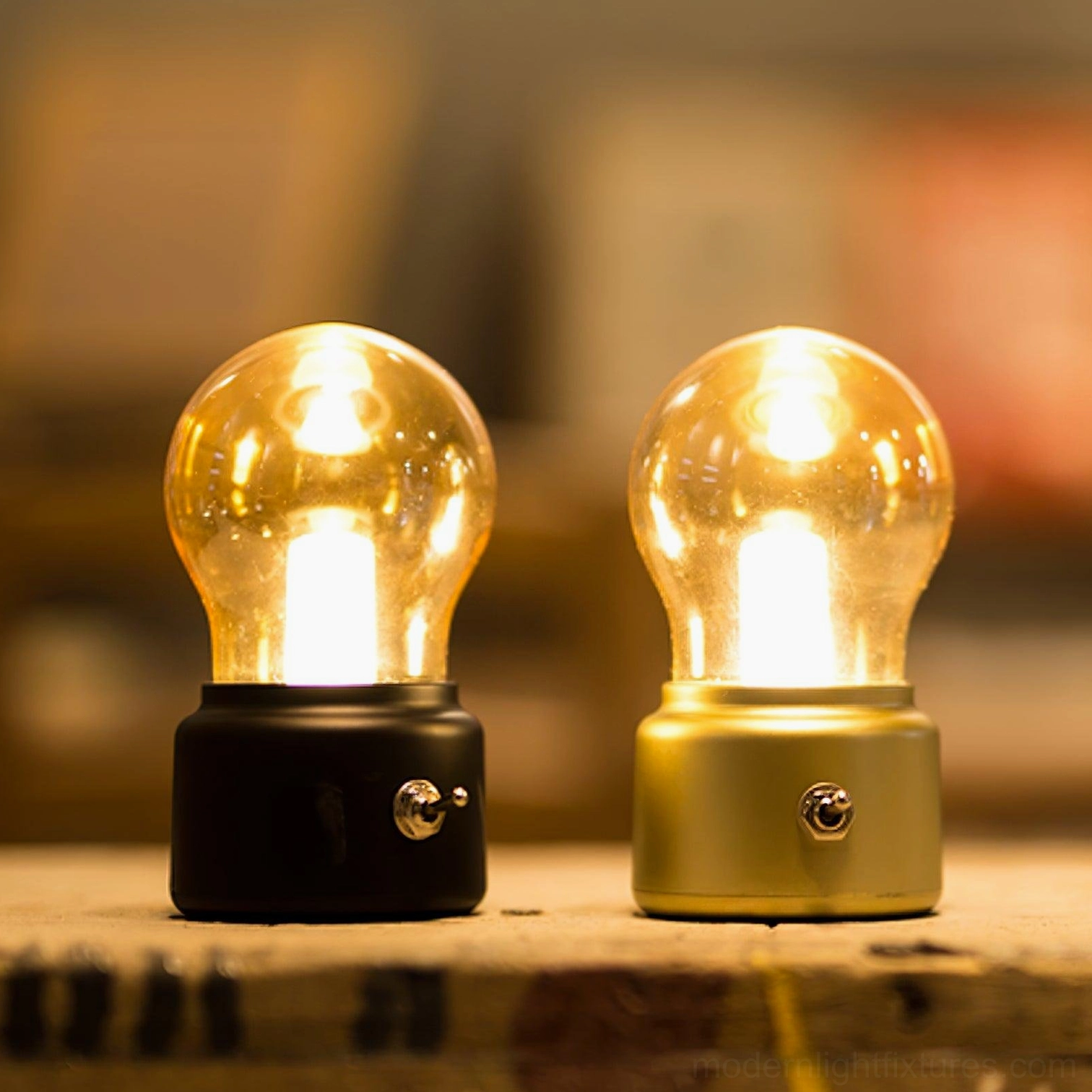 Matching pair of black and gold portable mini lamps with warm ambient glow on rustic wooden desk