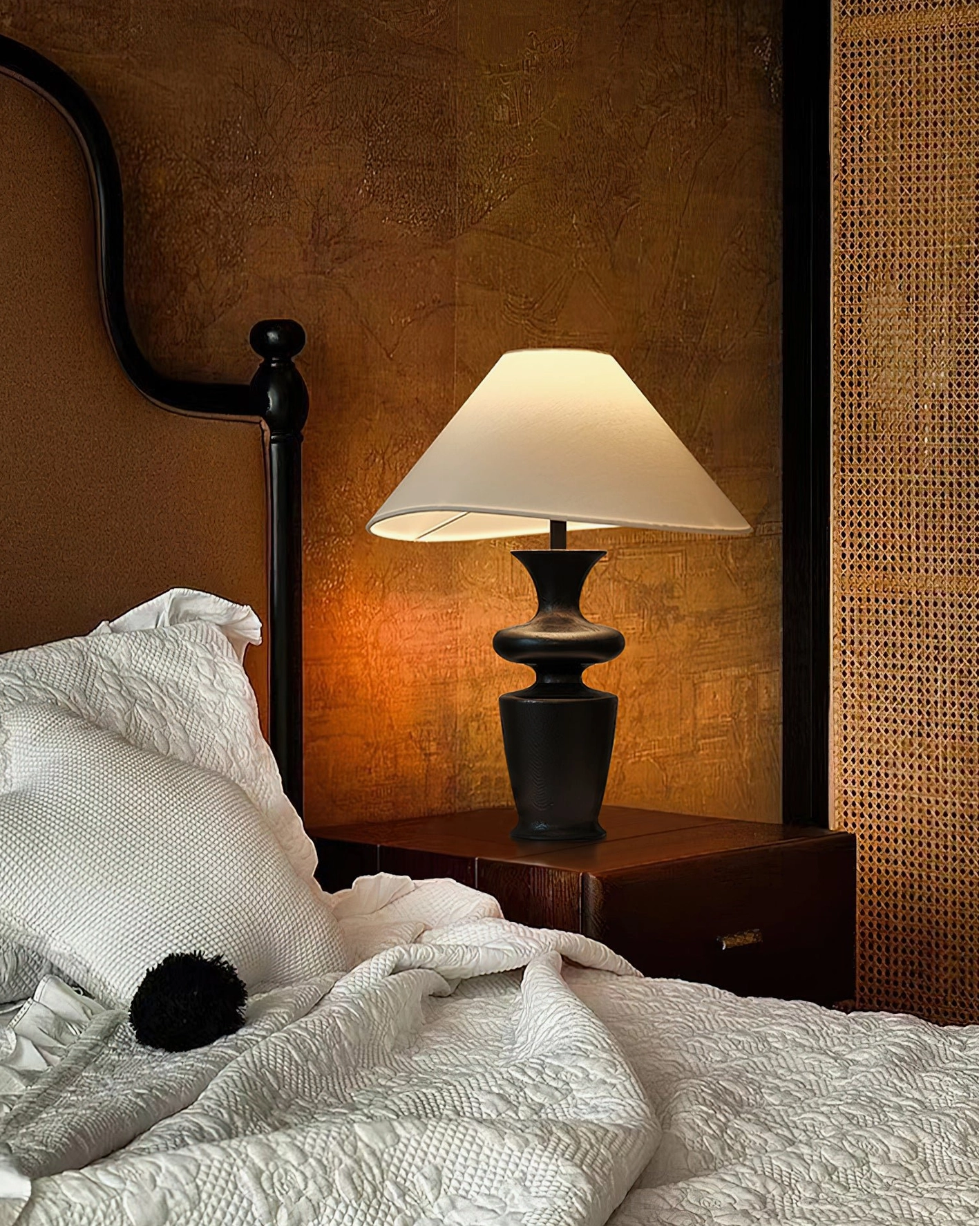 Minimalist bedside table lamp providing soft warm light in cozy master bedroom with white bedding, high-angle bedroom shot
