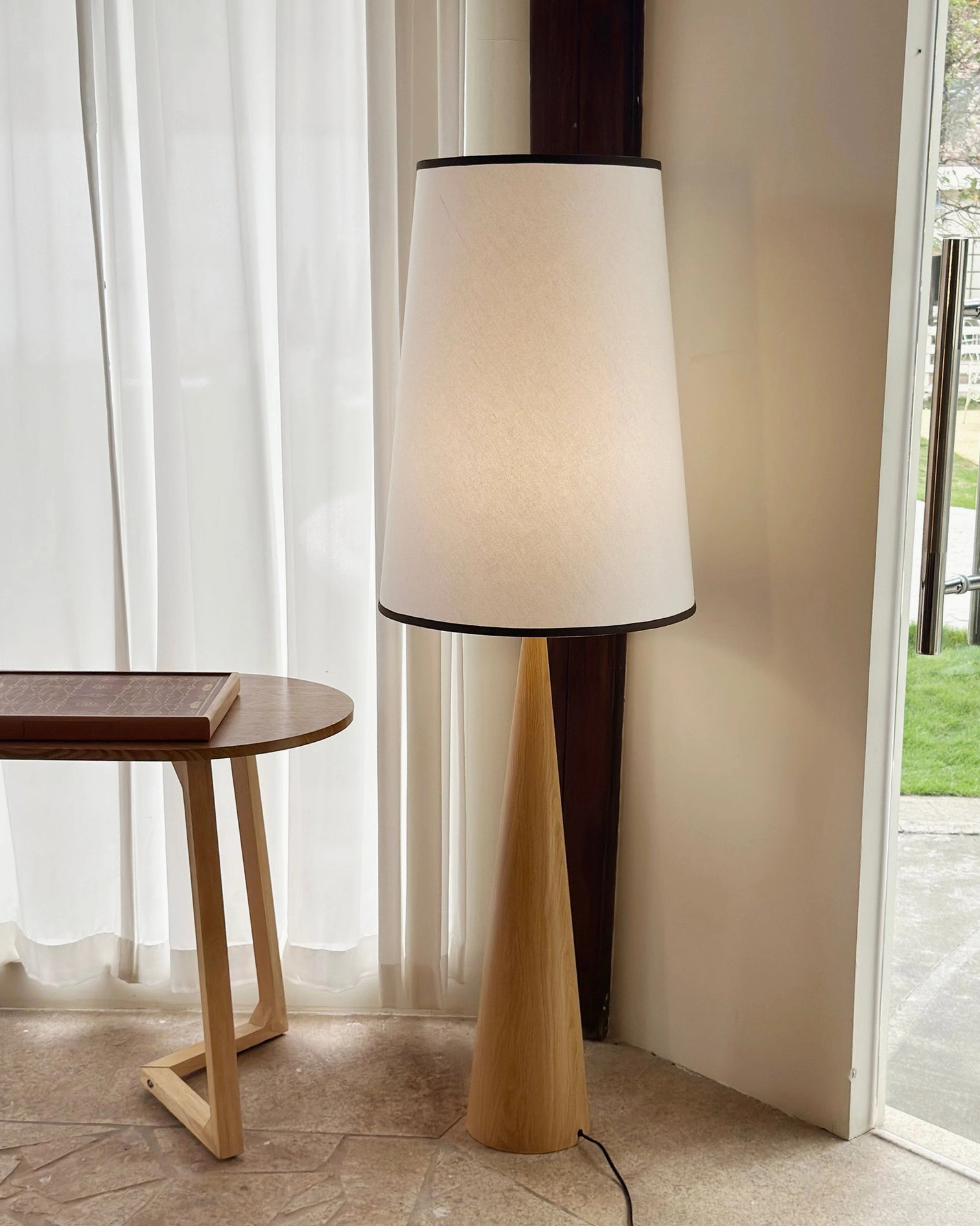 Contemporary tapered floor lamp with off-white shade near glass door and sheer curtains in minimalist room