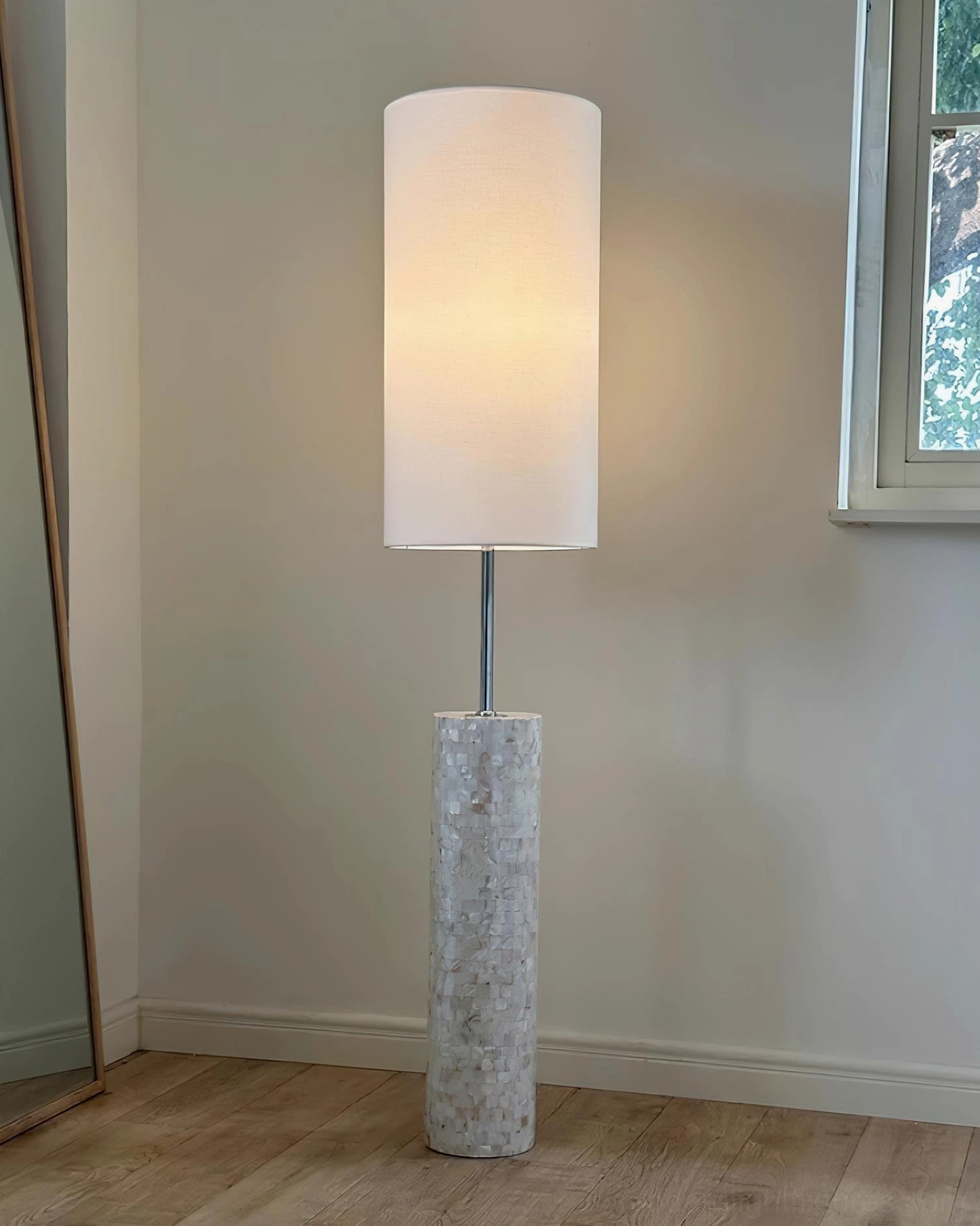 Contemporary minimalist floor lamp with white fabric shade against empty wall with mirror