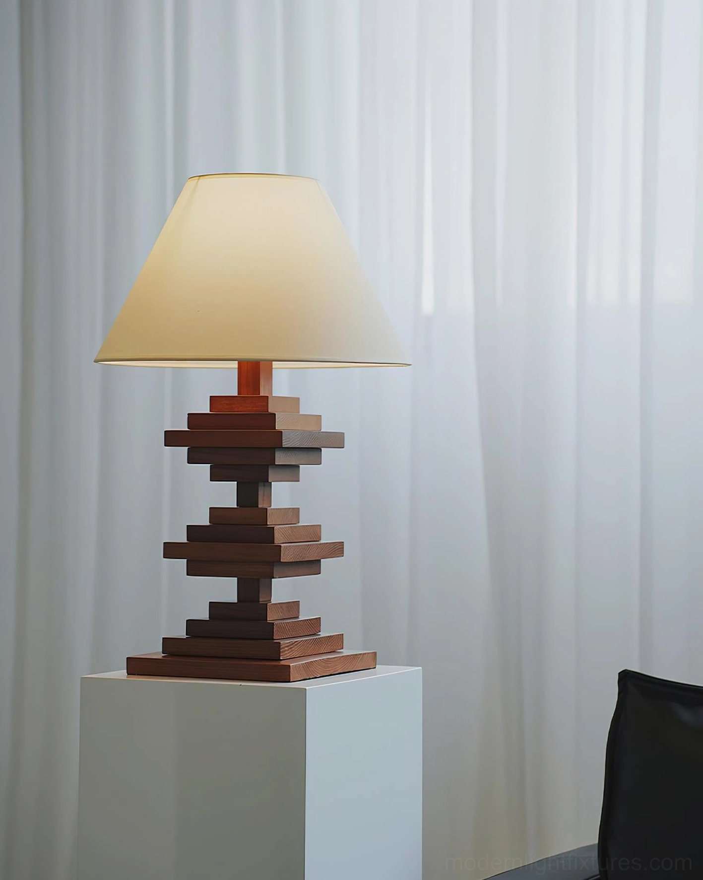 Modern geometric wooden tower table lamp in neutral interior with white pedestal minimalist curtains and contemporary styling