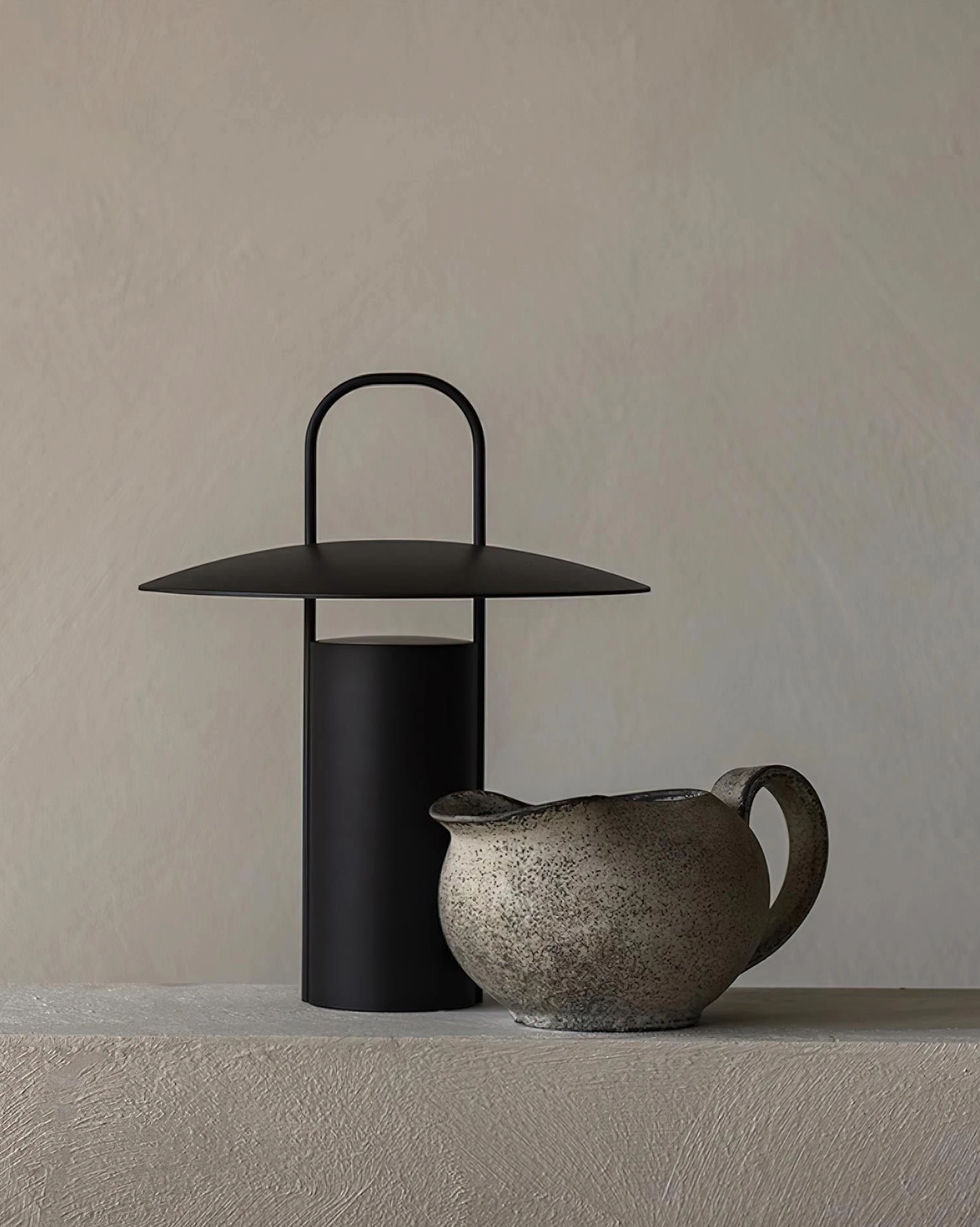 Matte black LED table lamp front view on minimalist display table with ceramic pitcher and modern home decor