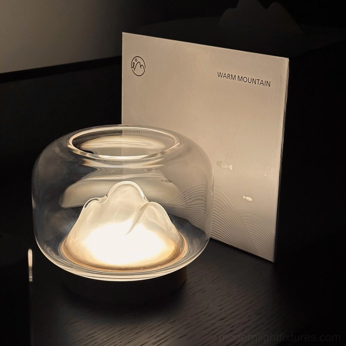Minimalist mountain glass table lamp high angle side view, clear dome design with packaged detail background