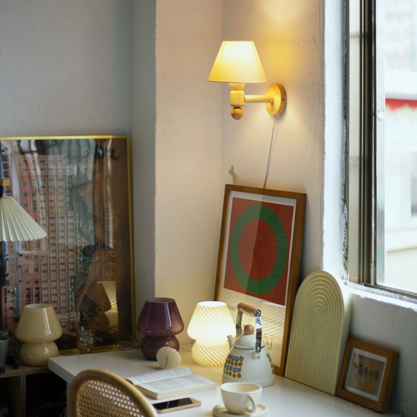 Contemporary wall lamp with lit cream shade mounted above home office desk with multiple decorative accessories