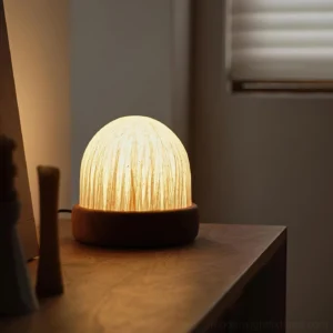Mireya contemporary table lamp glowing with warm 3000K LED light on wooden side table, low angle perspective