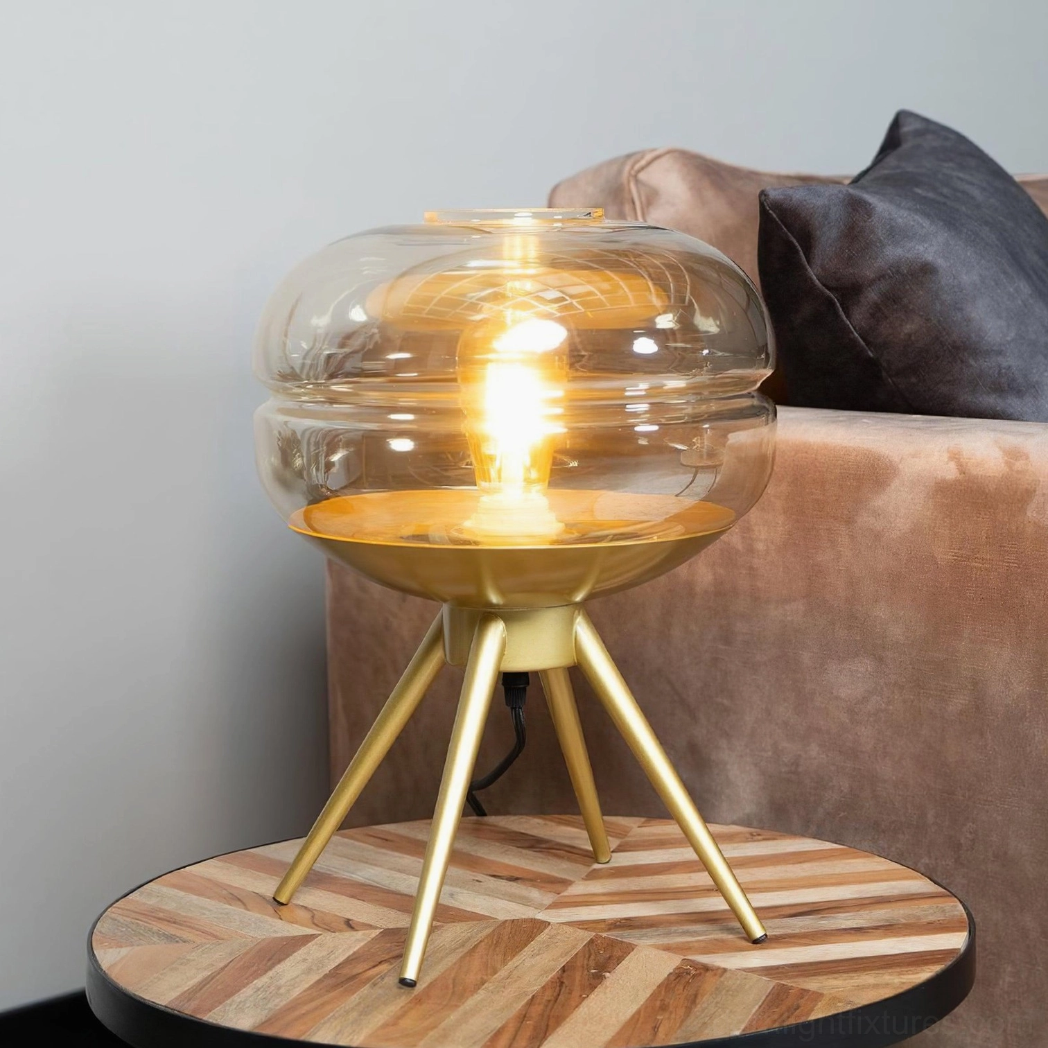 Illuminated amber glass tiered table lamp placed on modern living room side table with velvet sofa backdrop