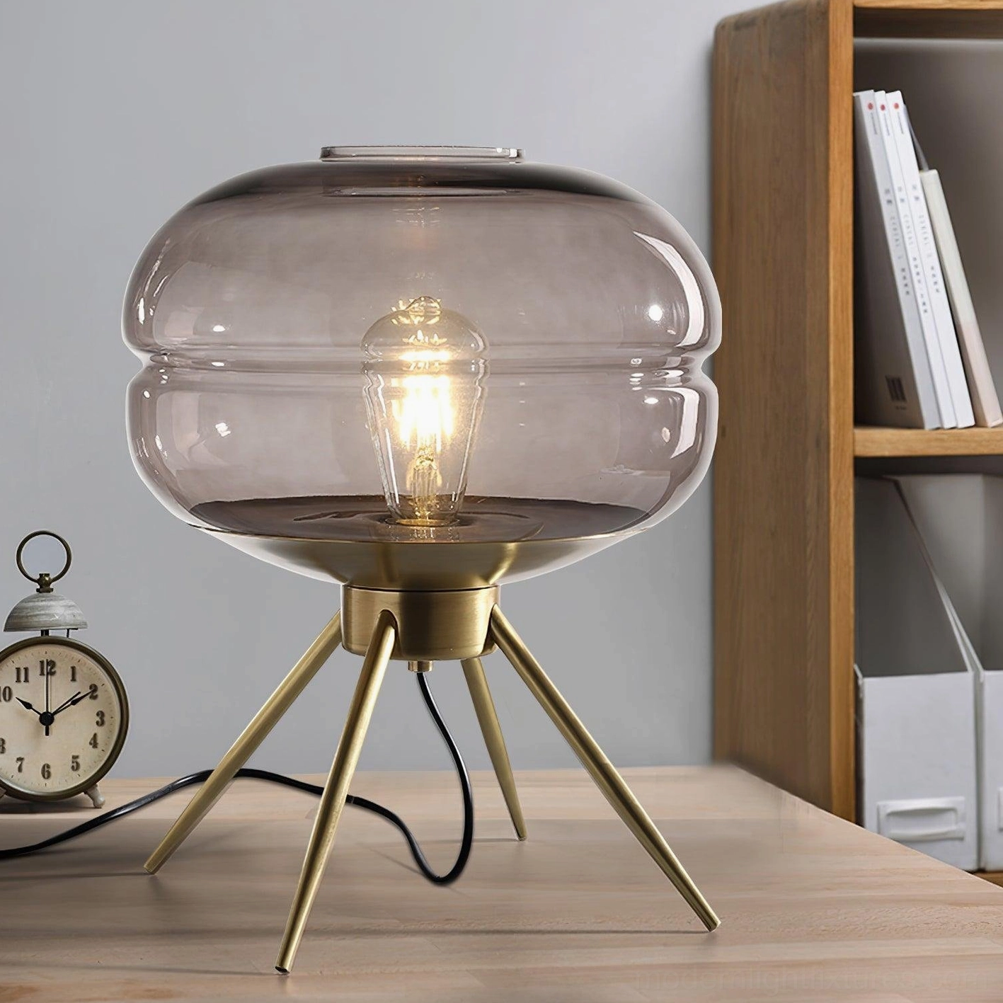 Smoke gray tiered glass table lamp with exposed vintage bulb on bedroom side table with clock and books