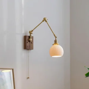 Model A compact swing arm wall sconce with white ceramic globe, mounted beside bedroom furniture
