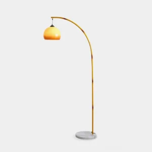 Modern arc floor lamp with yellow metal pole and caramel glass shade on white marble base - front view studio shot