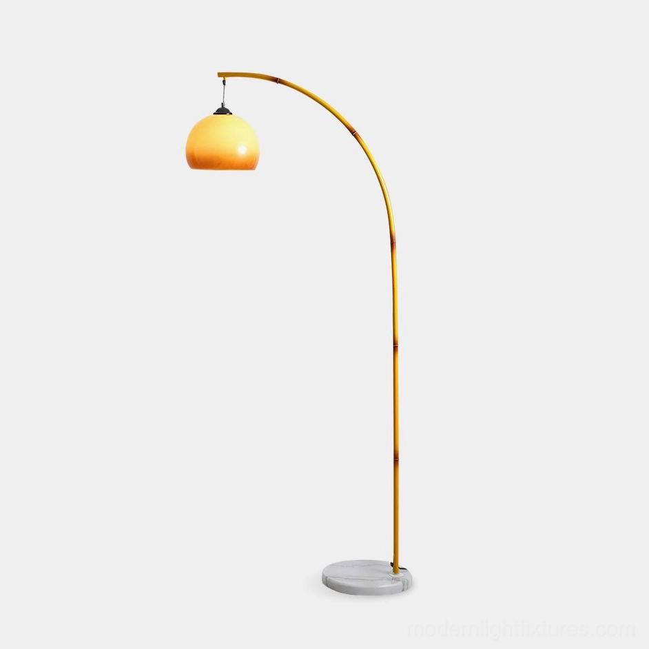 Modern arc floor lamp with yellow metal pole and caramel glass shade on white marble base - front view studio shot