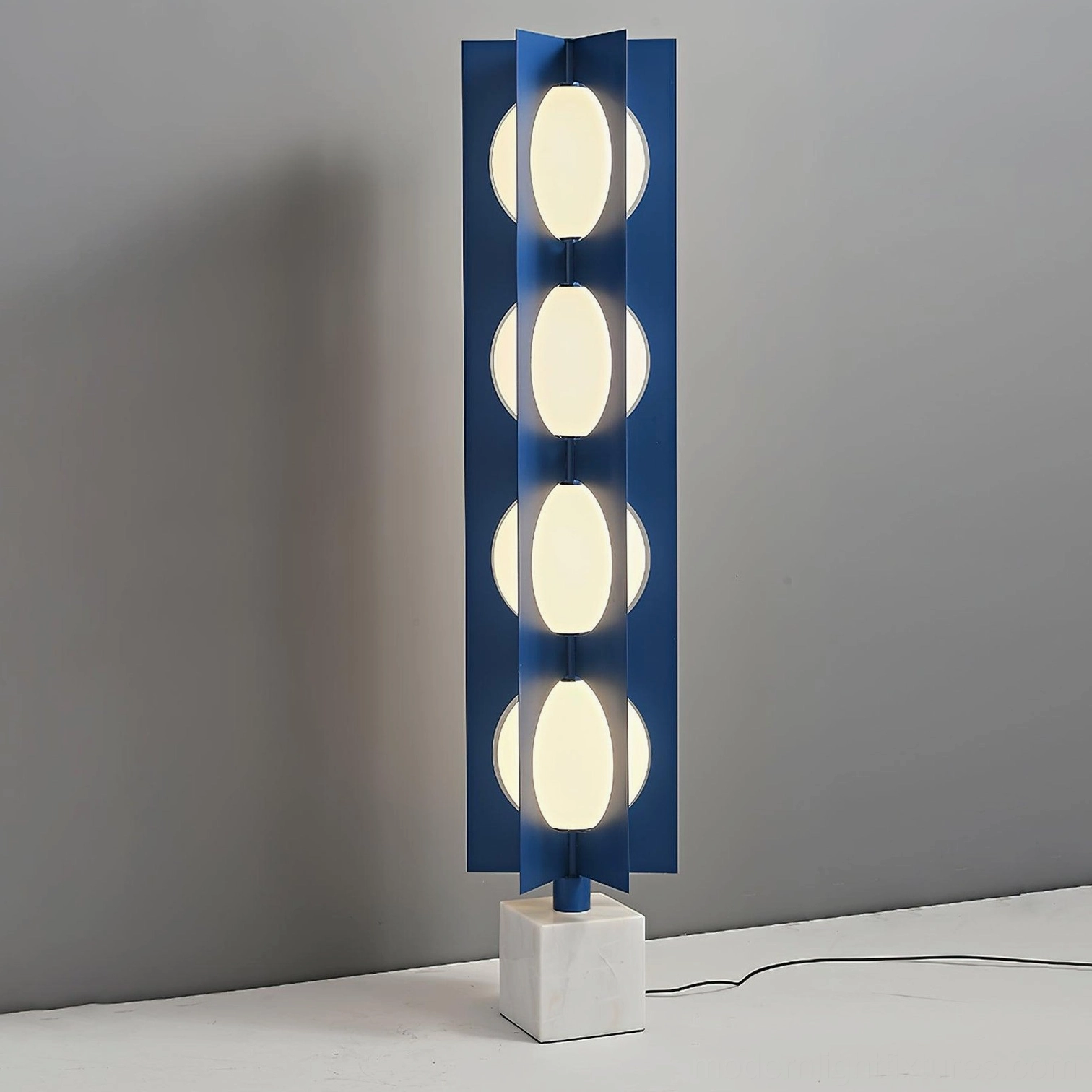 Contemporary blue glass floor lamp three-quarter view showing metal frame and powered cord with studio lighting